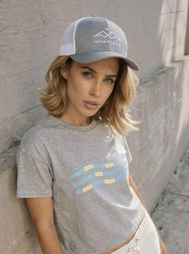 Casquette trucker NOWFIELD coloris gris et blanc portée dans un environnement outdoor au design minimaliste.